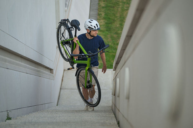 Een man loopt buiten een trap op met een groene CUBE fiets in de hand.
